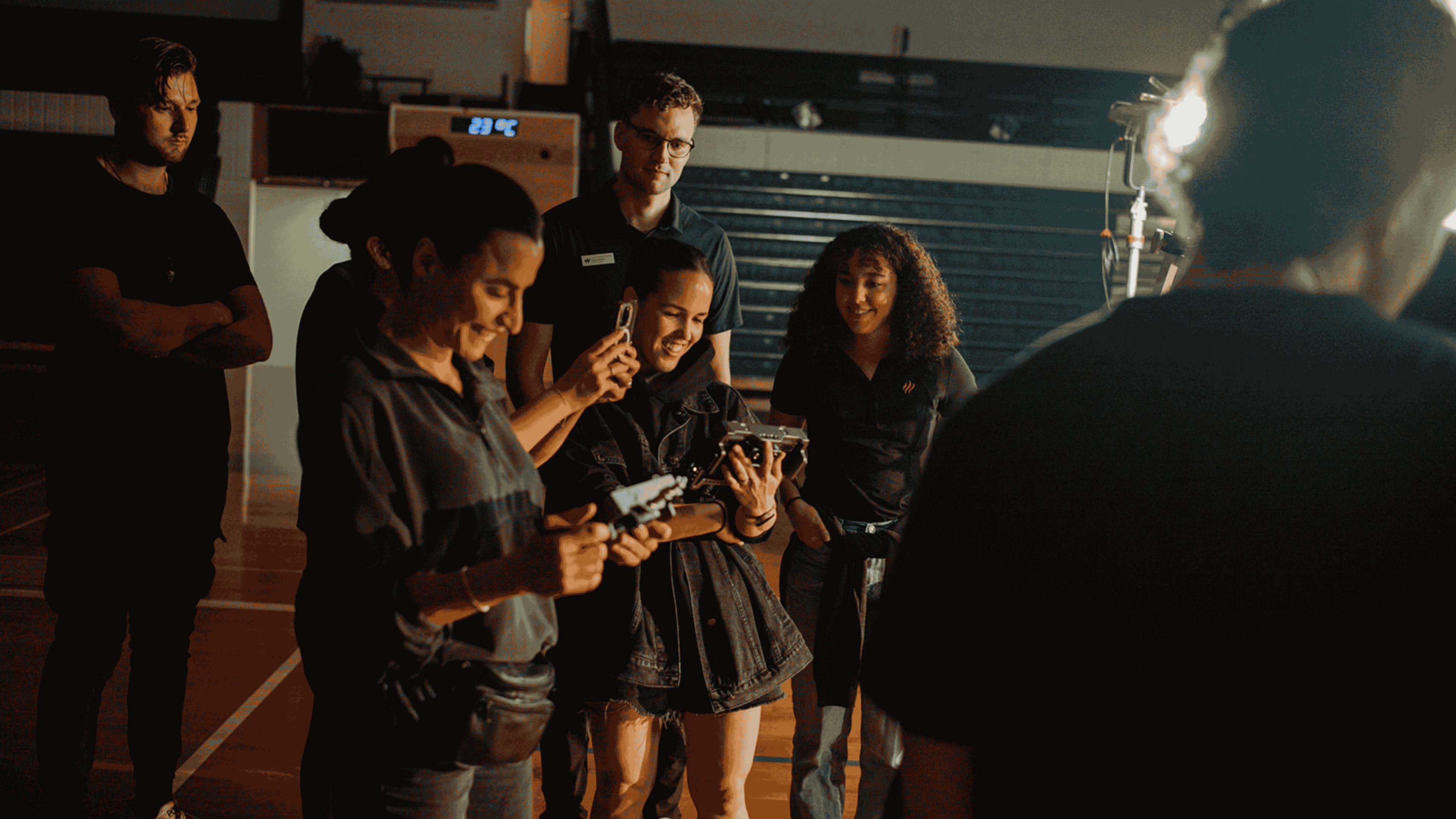 Group of people gathered indoors, smiling and examining small objects or devices in their hands under warm lighting.