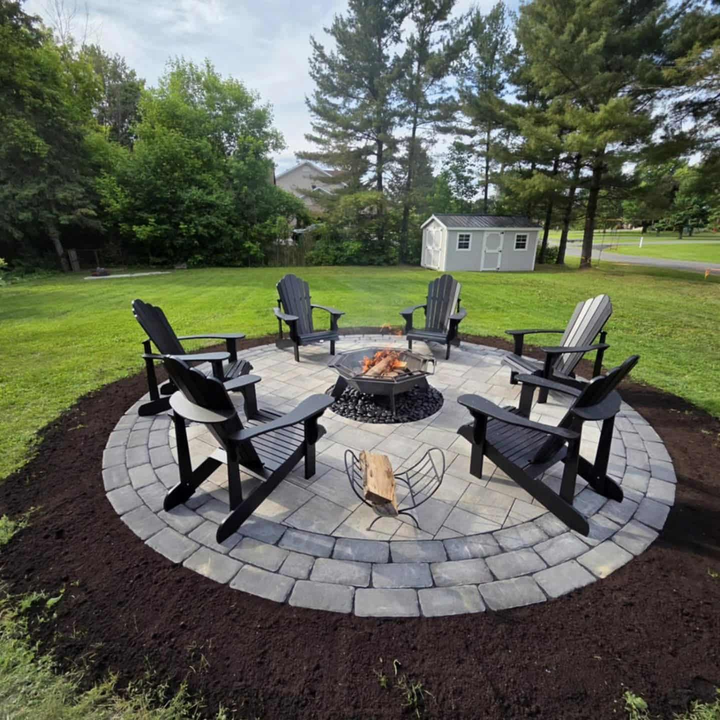 Round stone patio with fireplace in center with 6 adirondak chairs