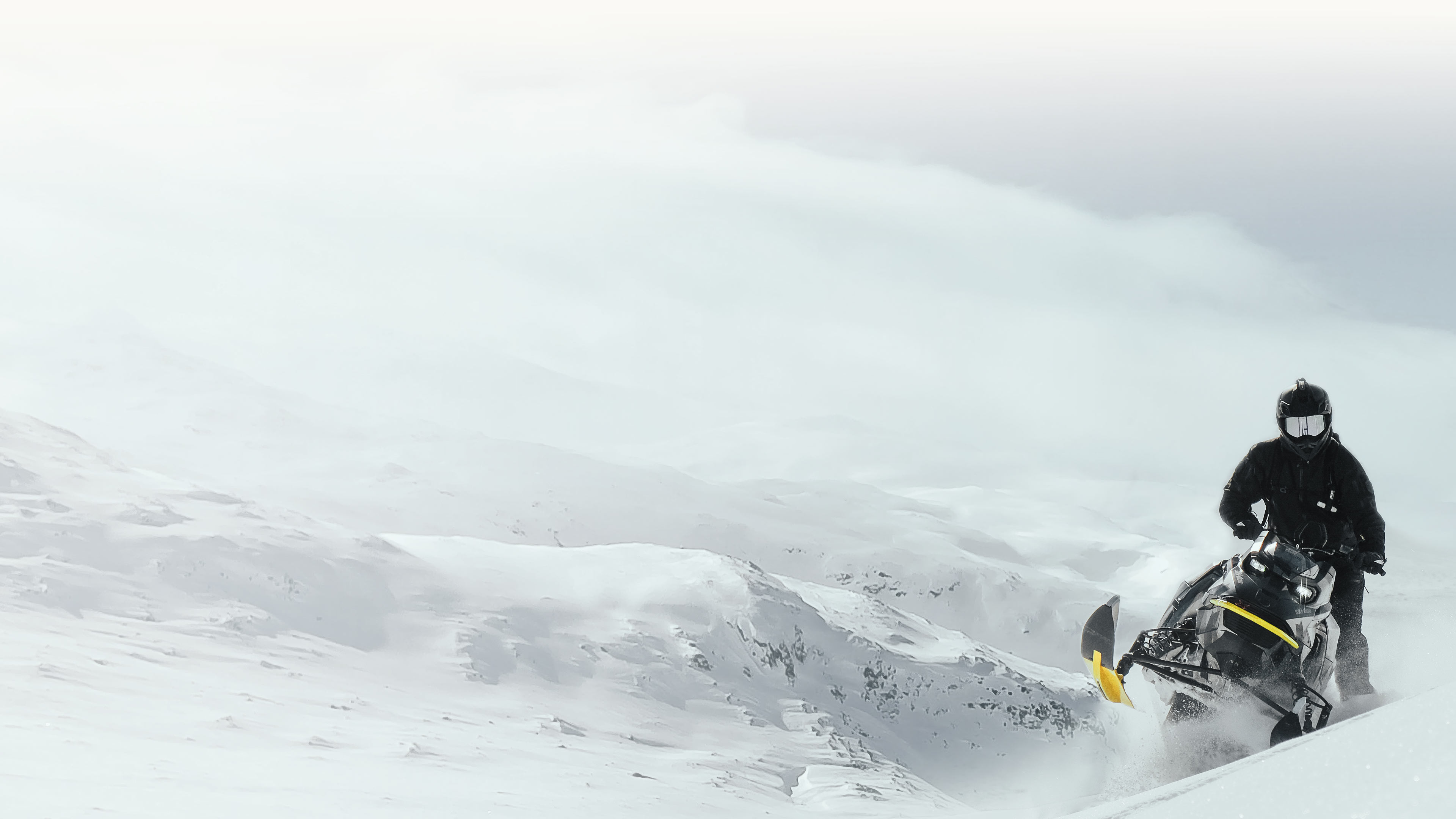 Man driving a snowmobile in an arctic scenery with powder snow flying