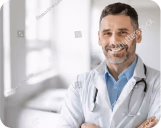 Smiling male doctor in white coat with stethoscope in bright medical office.