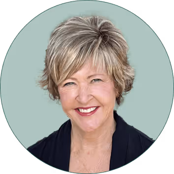 Smiling middle-aged woman with short blonde hair wearing a dark blazer on a muted green background.