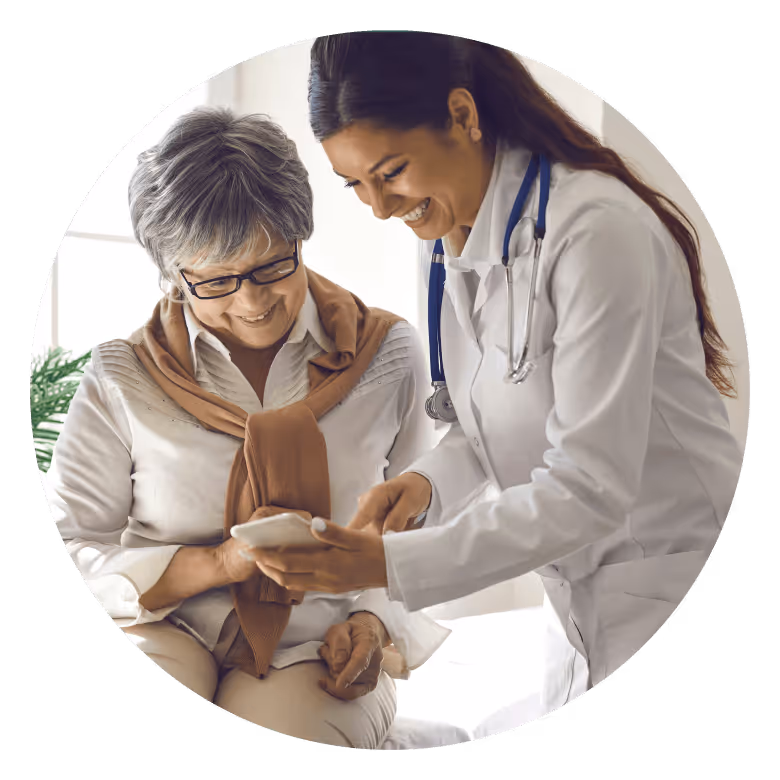 Smiling female doctor showing smartphone to elderly woman with glasses and scarf.