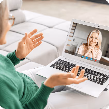 Person in green sweater having a video call with a smiling woman displayed on a laptop screen.