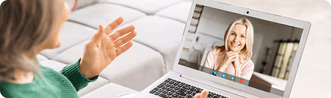 Person in green sweater video chatting with smiling blonde woman on a laptop screen.