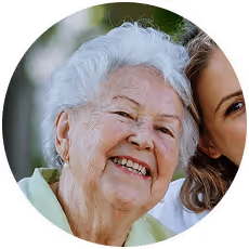 Smiling elderly woman with white hair next to a younger woman in an outdoor setting.