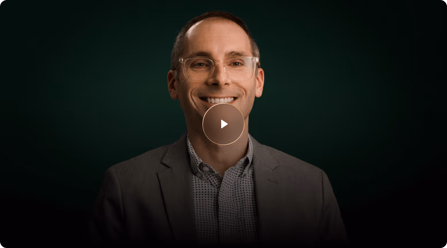 Smiling man wearing glasses and a suit jacket with a green background and video play icon.