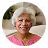 Smiling elderly woman with short white hair wearing a pink top against a light background.