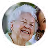 Smiling elderly woman with white hair wearing a light blue top and earrings.