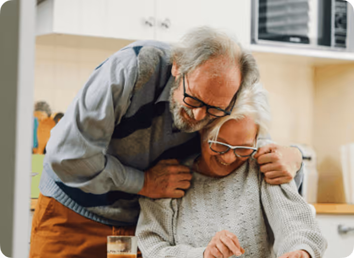 Elderly couple smiling and hugging in a cozy kitchen setting.