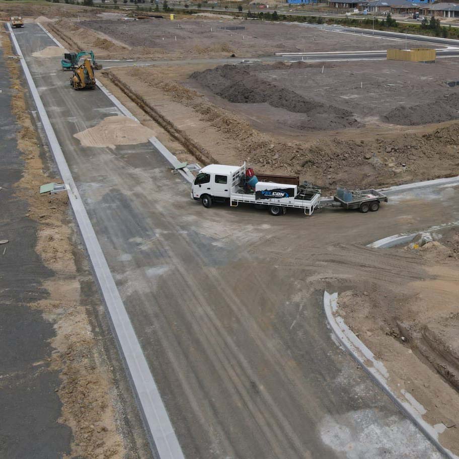 Land development gutter concrete with a truck driving on the road completed by Melbourne Kerb & Channel Concrete specialists, Velcon