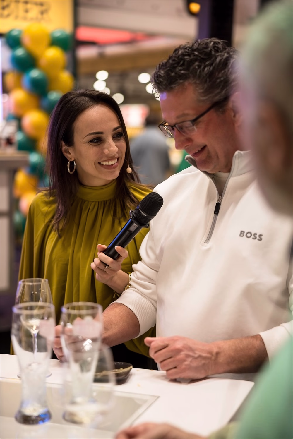 Vrouw met microfoon praat met man in een witte trui met het woord BOSS erop.
