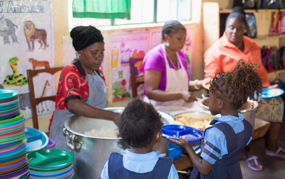 Essensausgabe in der Maria Regina Schule in Sambia: Mitarbeitende geben warmes Essen an Schulkinder aus.