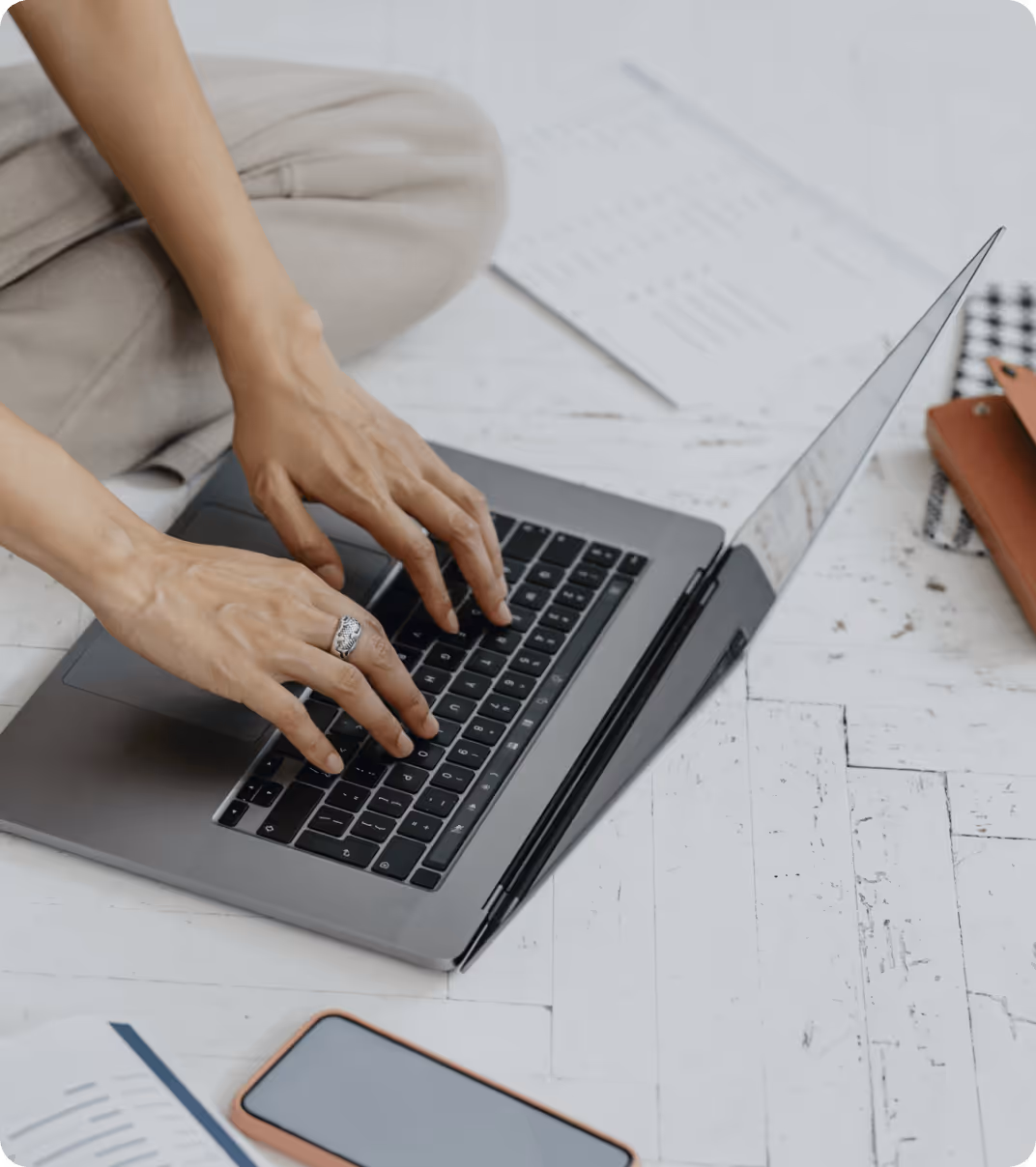 Person typing on a laptop with a smartphone and documents on the table