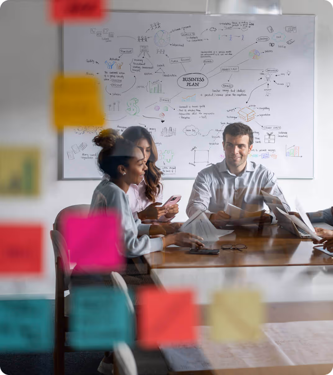 Team collaborating in a conference room with sticky notes on glass and a business plan brainstorming diagram on a whiteboard