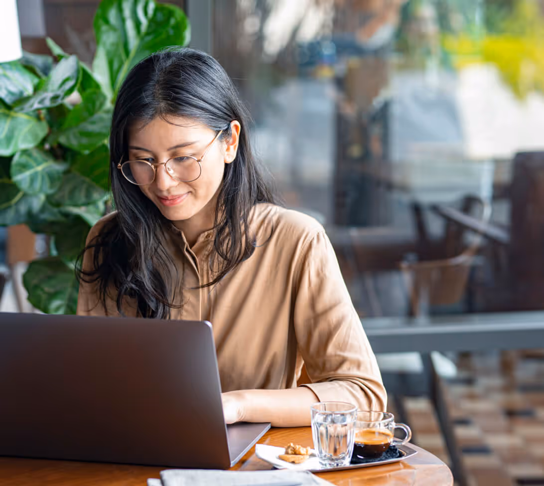 Professional working on a laptop at a café table with coffee and snacks, representing remote work, productivity, and modern digital workspace."