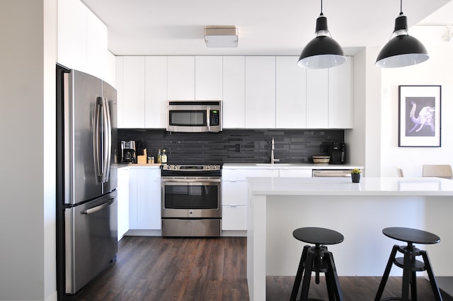 Cuisine avec armoires blanches, frigo noir et chaises noires.
