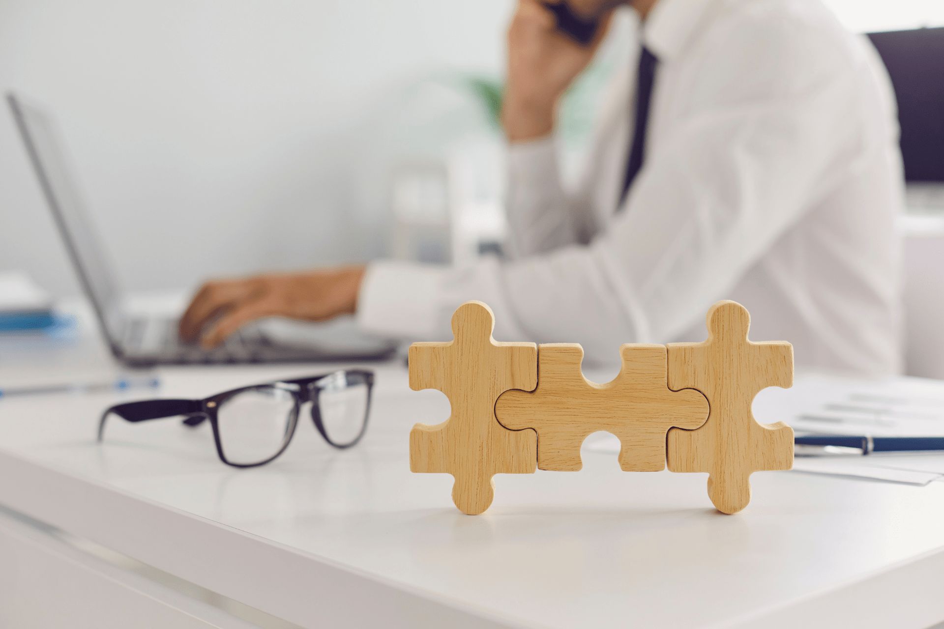 A person in the background working on a laptop and three jigsaw puzzle pieces in the foreground 