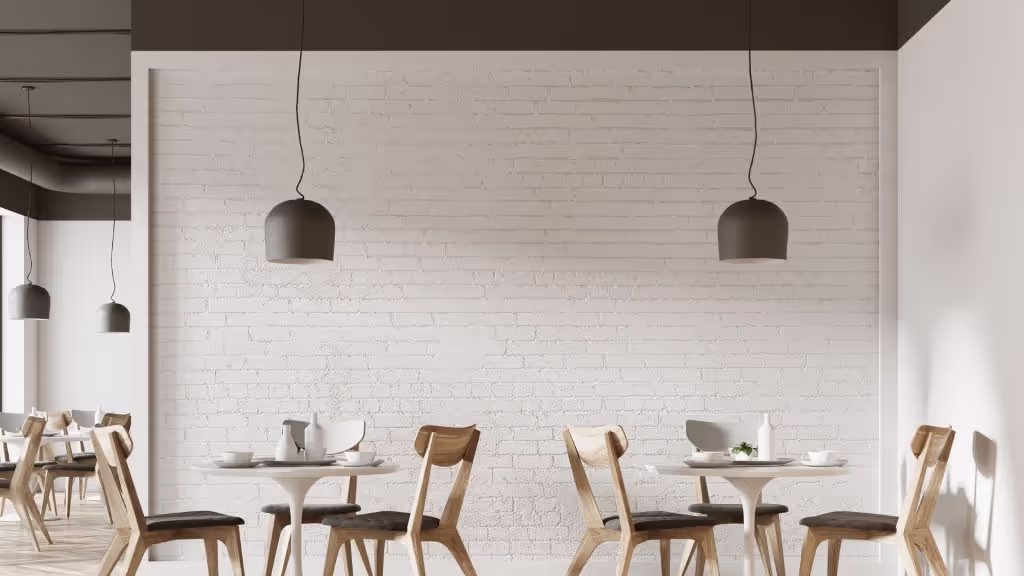 A minimalist cafe featuring light wood chairs, white brick, white tulip tables, and black hanging ceiling fixtures.