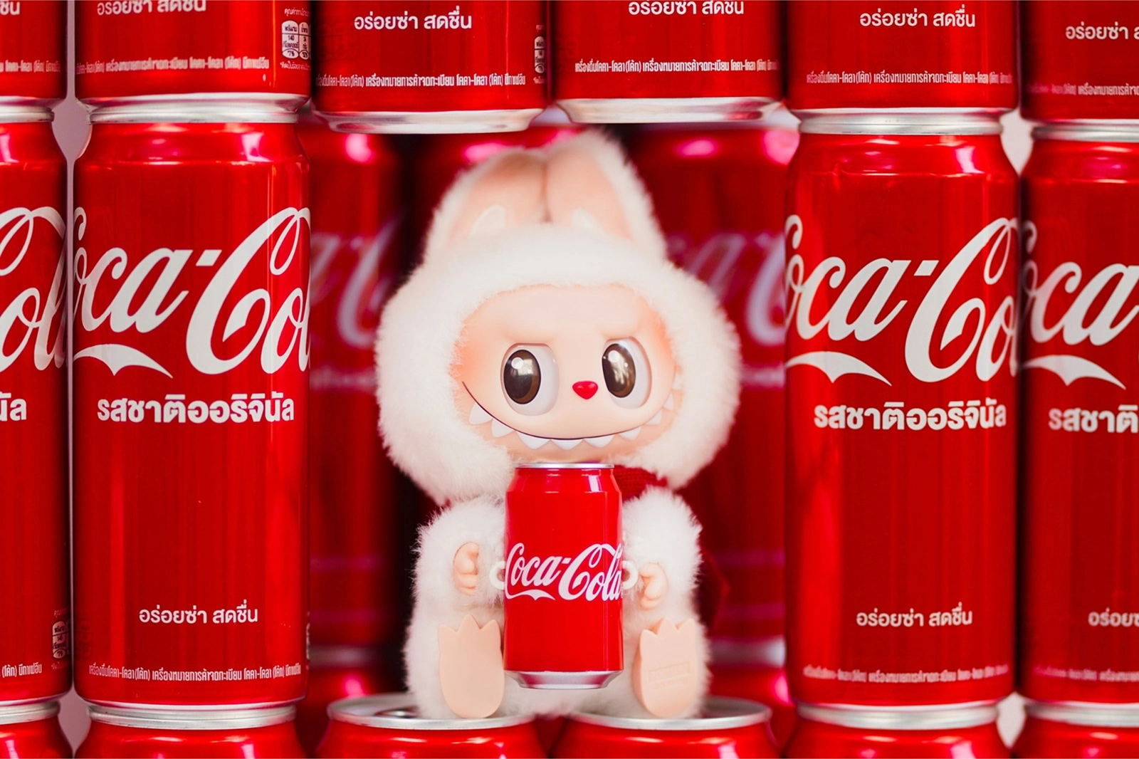 A white Labubu doll holding a Coca-Cola can, surrounded by red Coca-Cola cans, a creative product collaboration between Pop Mart and Coca-Cola.