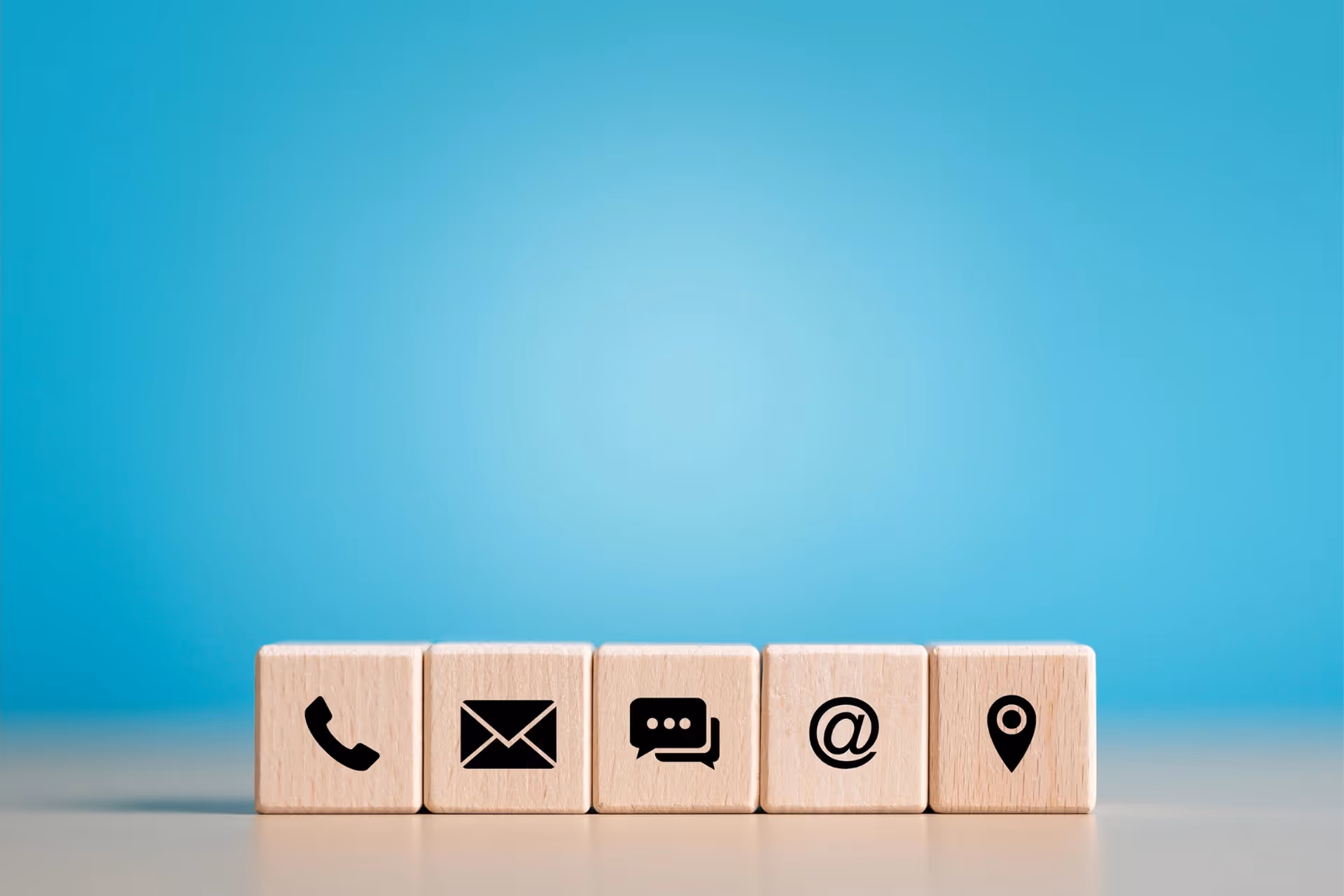 Five wooden blocks sit on a desk, each with a different contact us type logo.