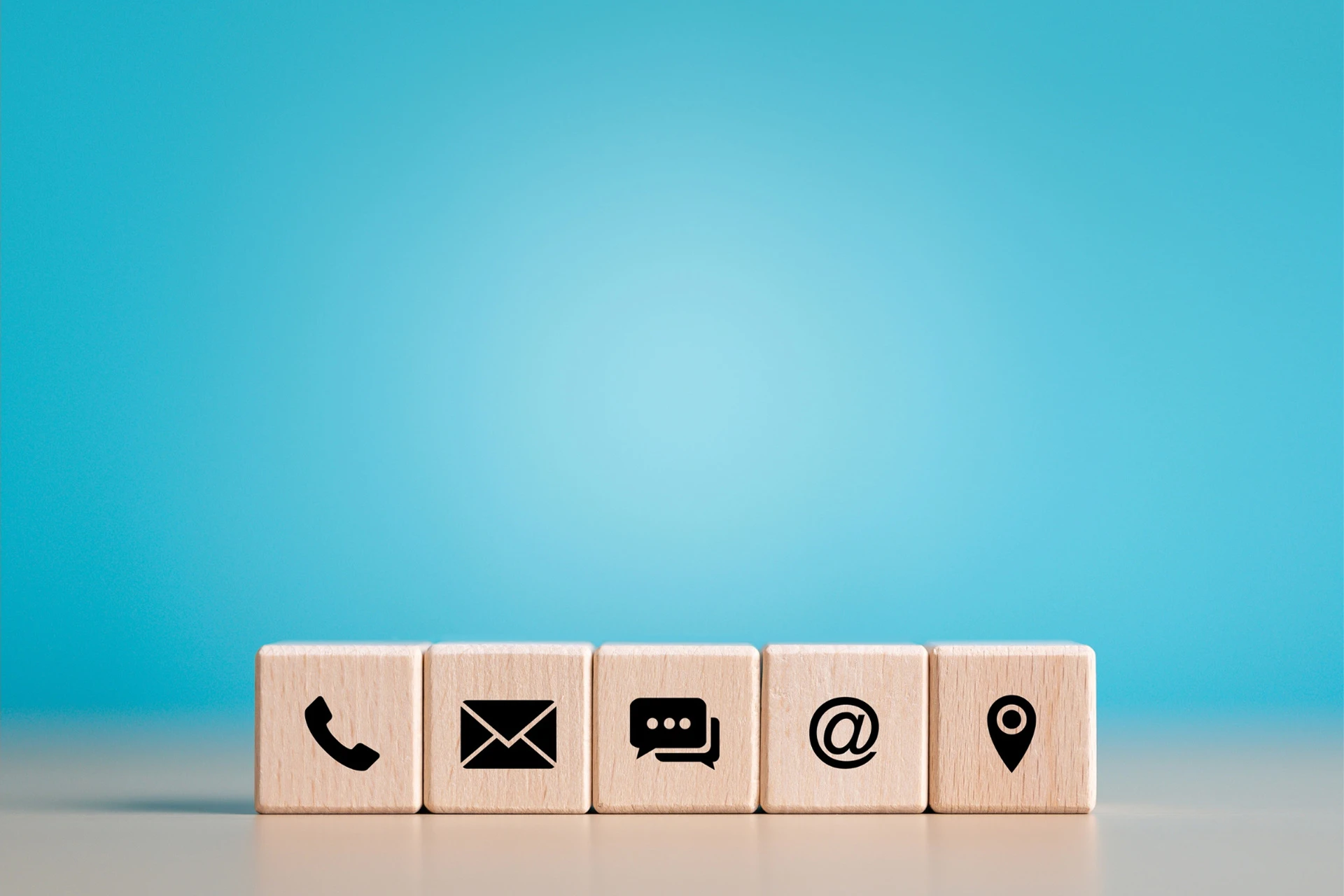 Five wooden blocks sit on a desk, each with a different contact us type logo.