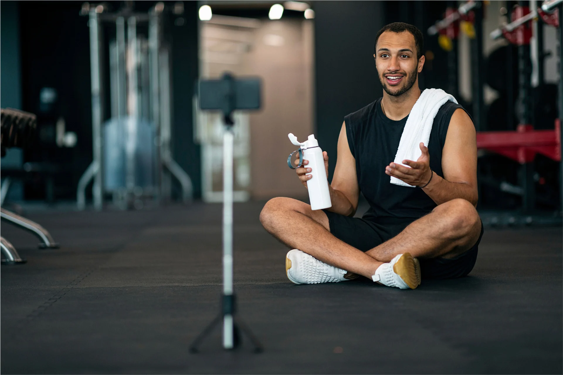 A student athlete filming content while sitting crisscross on a gym mat