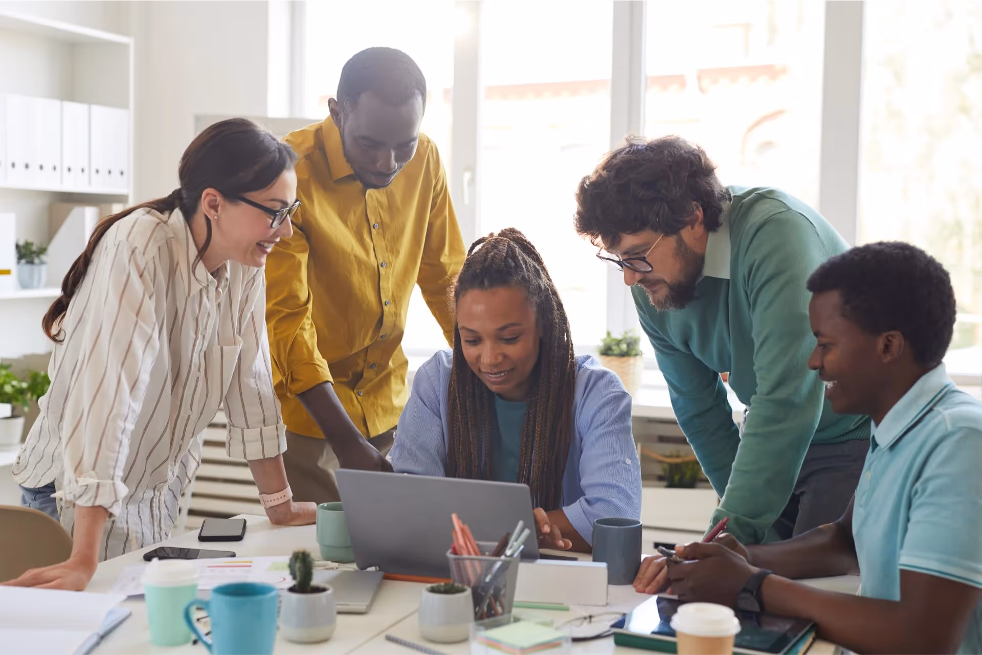 A group of marketers working together, huddled over one employee on her laptop 