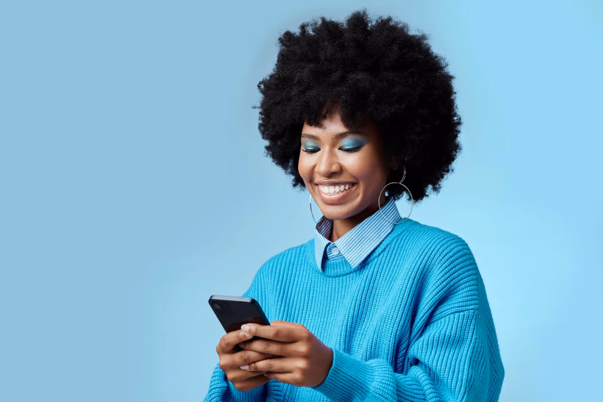 A woman in a blue sweater holds a phone and smiles at her personalized email.