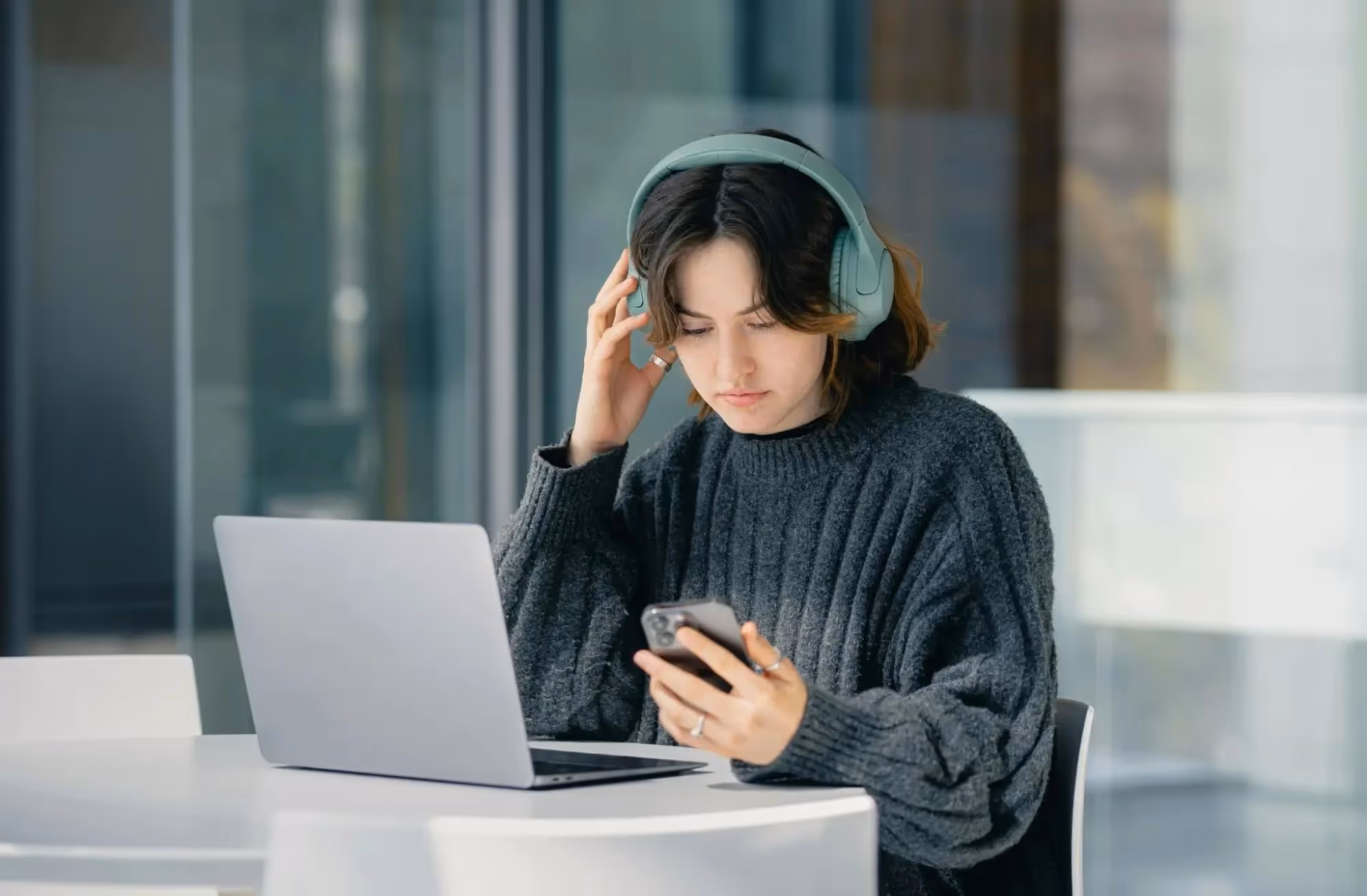 A female student with headphones on and laptop in front of her, a phone in her hand.