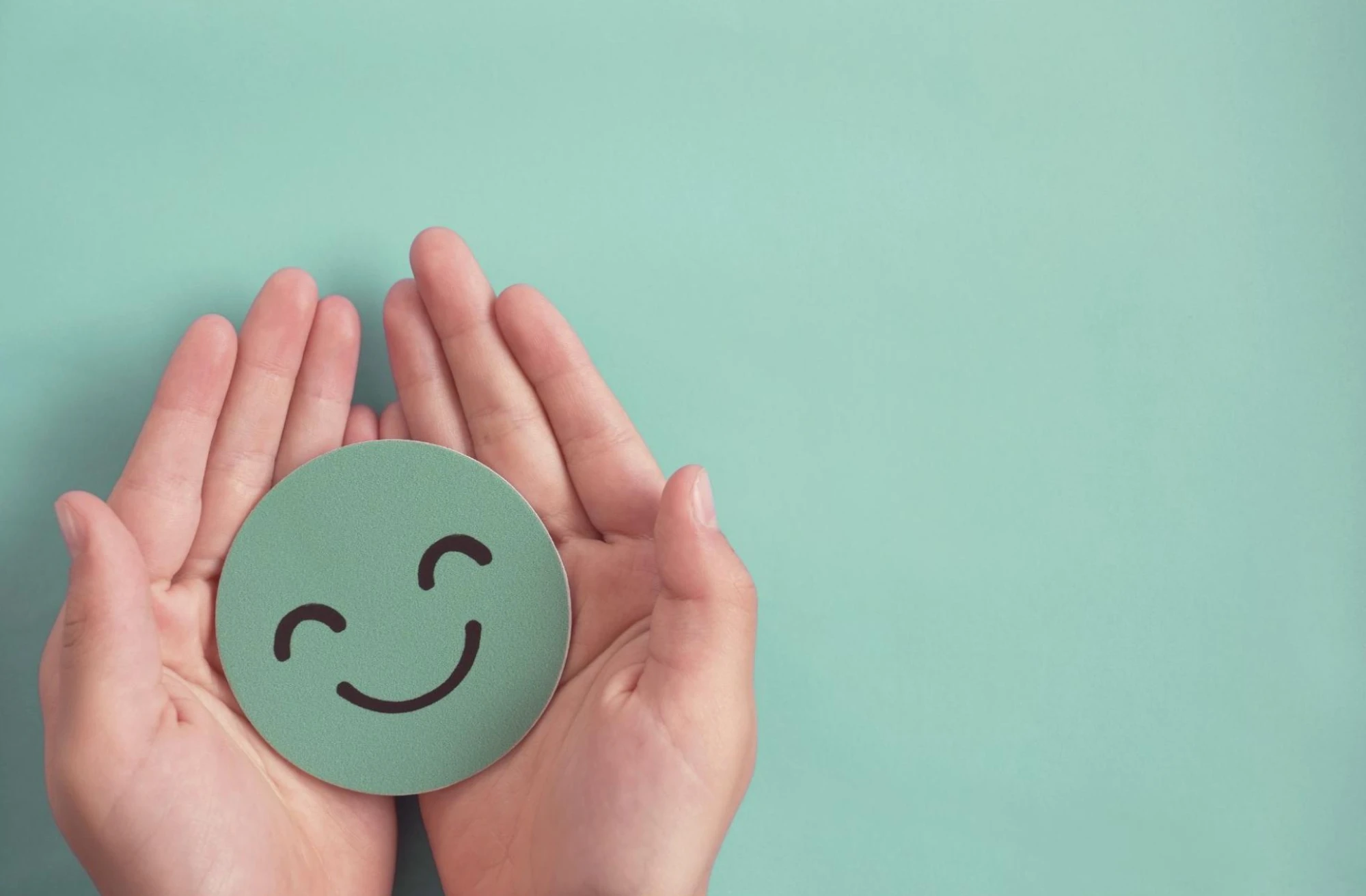 Hands holding a green circle with a smiley face on it.