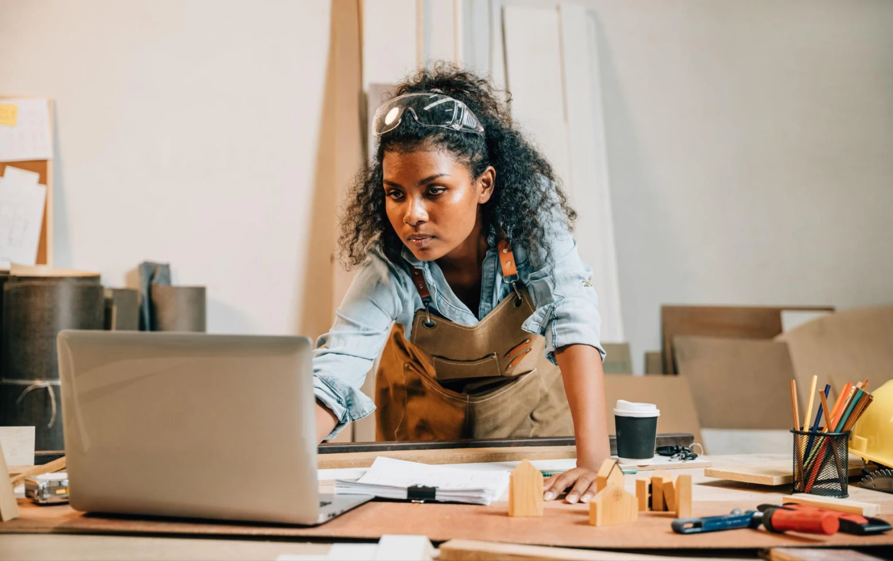 A female contractor checks her laptop over a table covered in papers and other items.