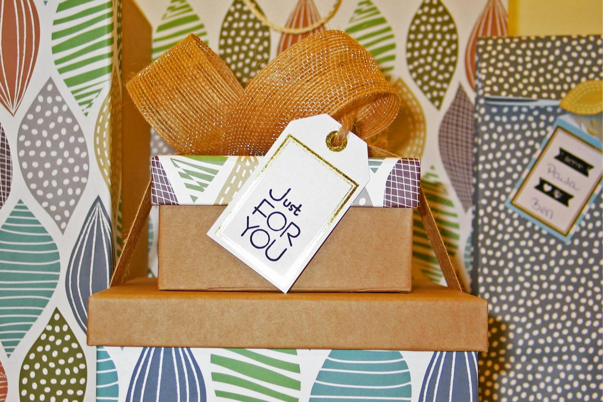 A small stack of gift boxes with patterned wrapping, a gold ribbon, and a tag that says “Just for you”