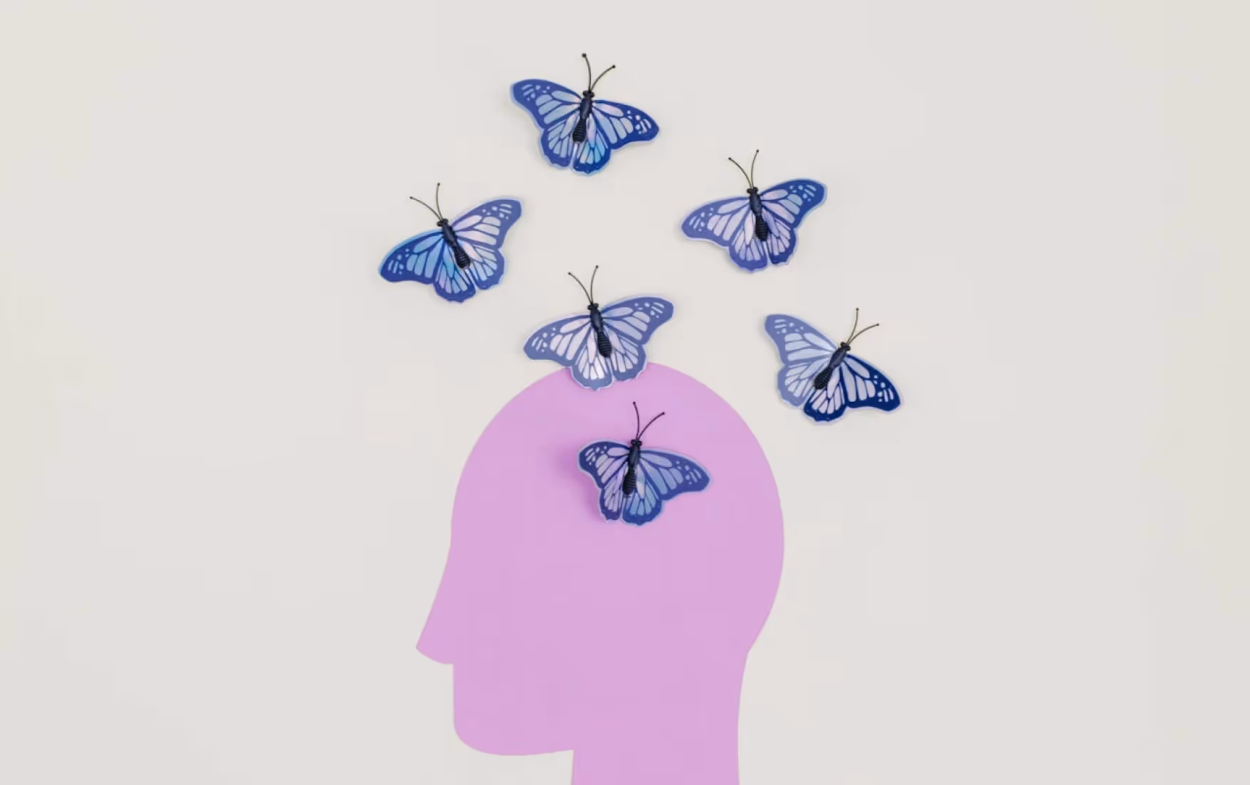 Purple silhouette of a head with blue paper butterflies appearing to flutter out from the top.