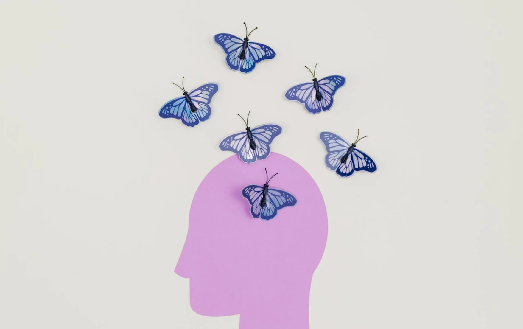 Purple silhouette of a head with blue paper butterflies appearing to flutter out from the top.