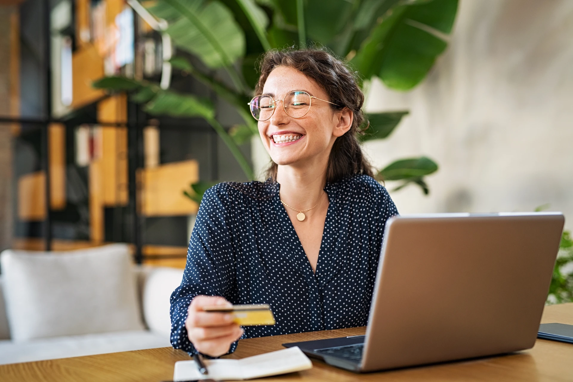 A smiling woman holding a credit card while using her laptop, happy after making an online purchase