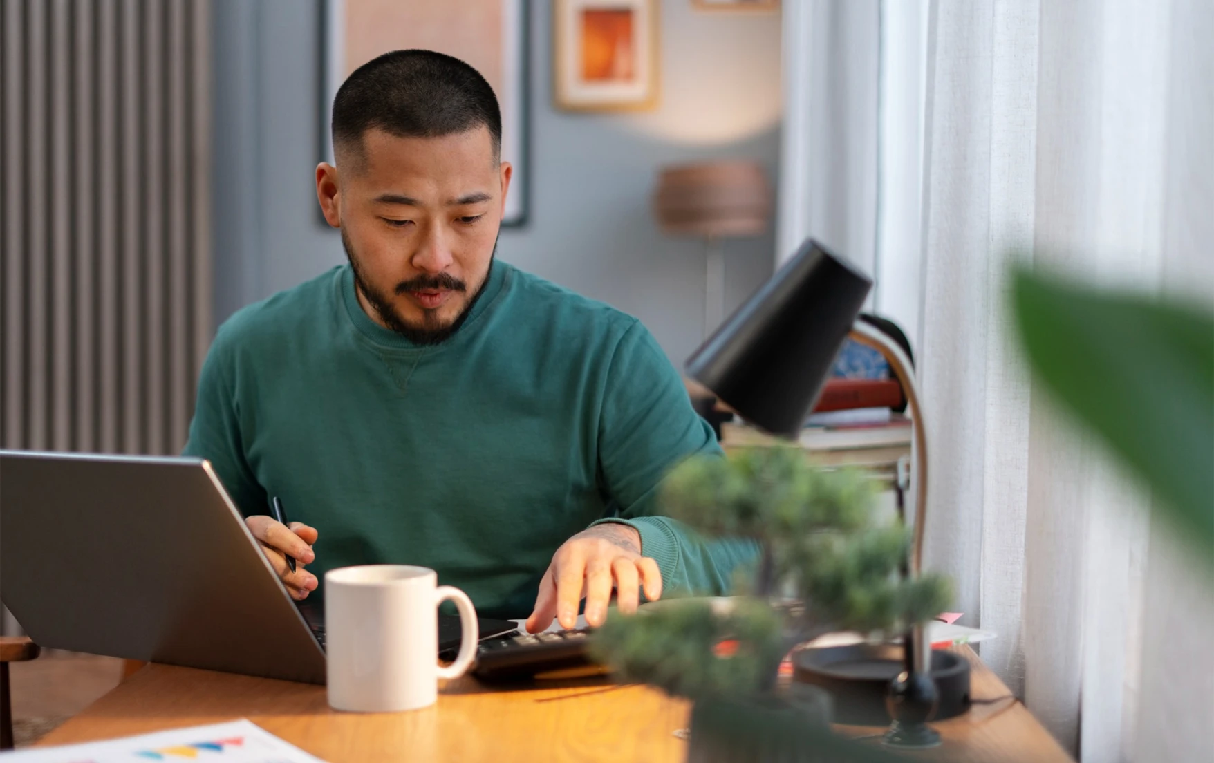A man in a green sweater at a desk using a laptop.