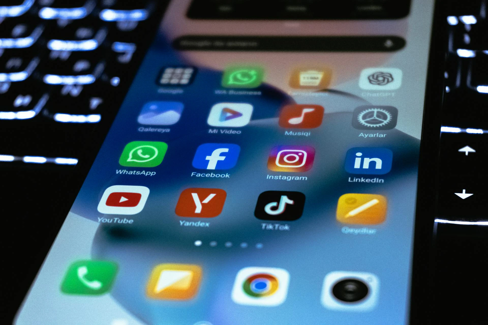 A smartphone placed on top of a computer keyboard, with its home screen displaying social media icons.