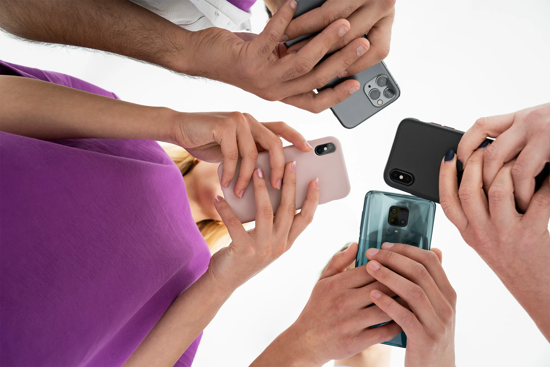 Four people holding smartphones in a circle, shot from below. The atmosphere is collaborative, with diverse hand positions and colorful phone cases.