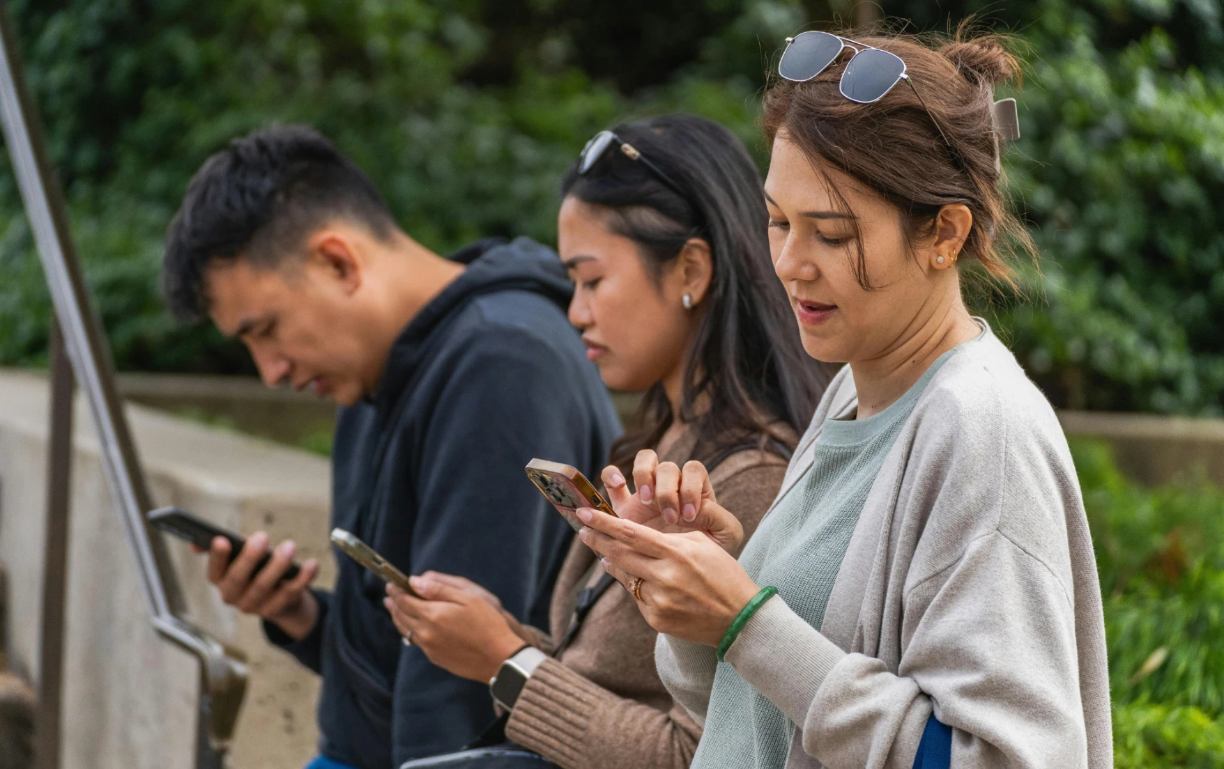 Three millennials using their phones while in a park