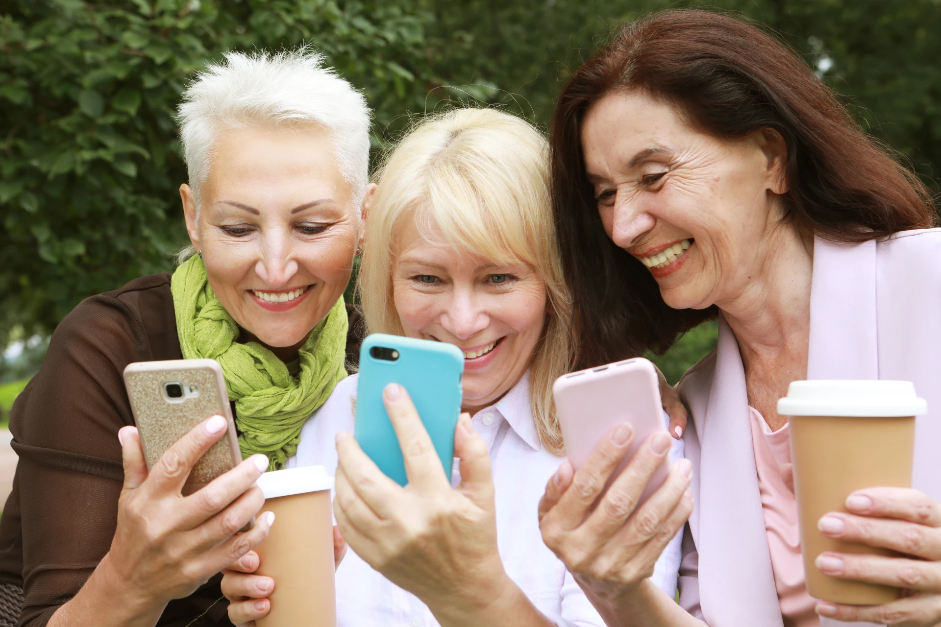 Three Generation X women smiling while looking at their phones