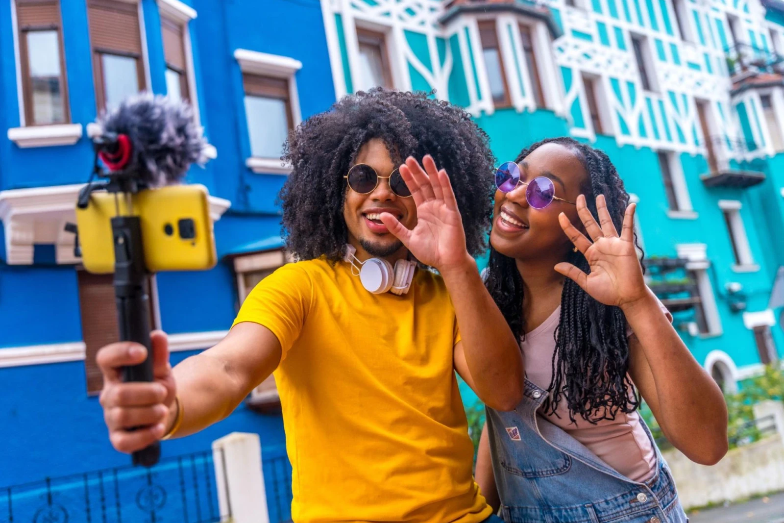 A young man and woman pose for a photo outdoors, with a blue-and-white building in the background.