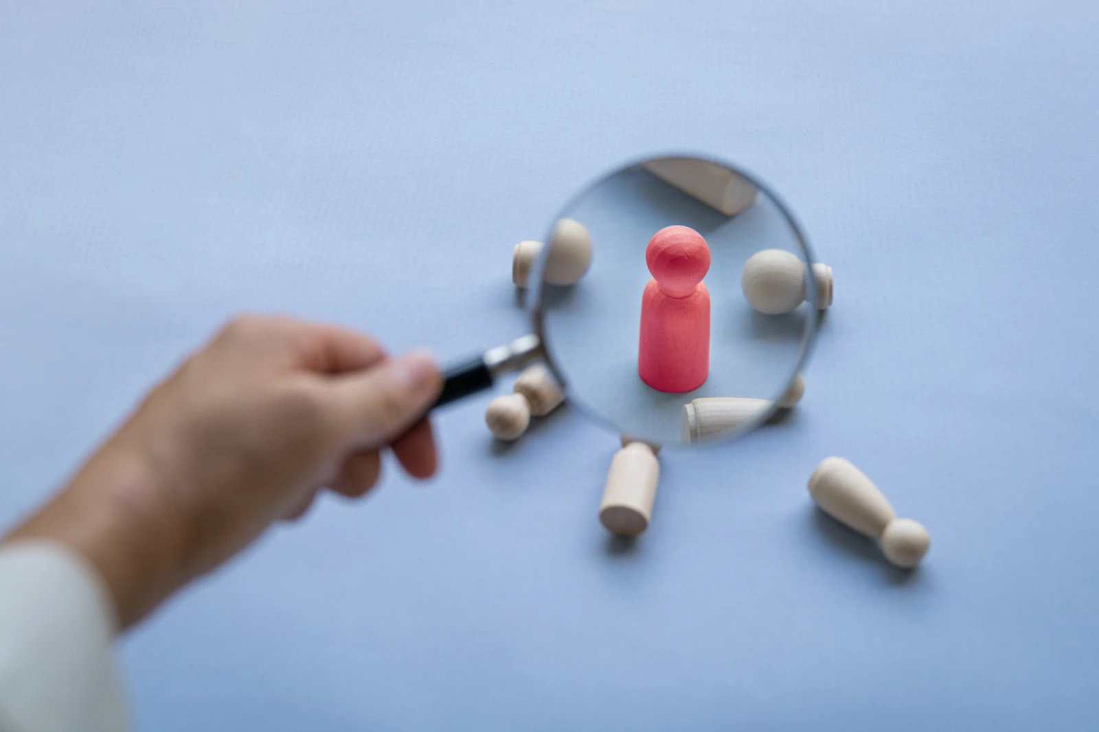 A hand focusing a magnifying glass on a human-shaped pink wooden block