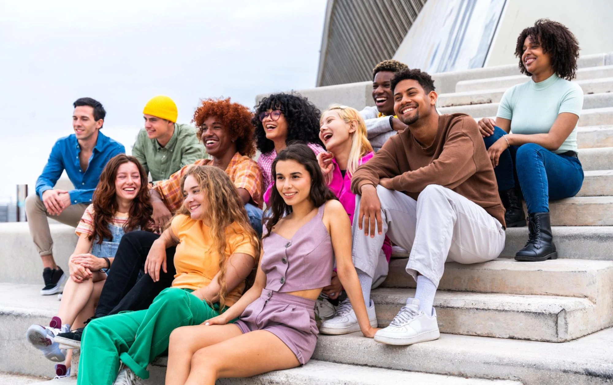 A group of eleven young adults are sitting on concrete stairs, laughing and smiling.