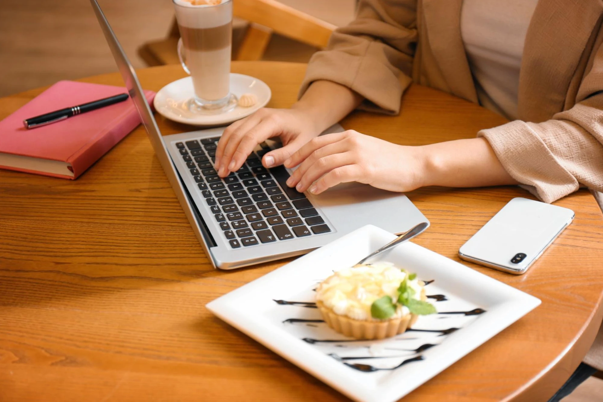 A content creator working on a laptop with a plate of pastry and a cup of coffee