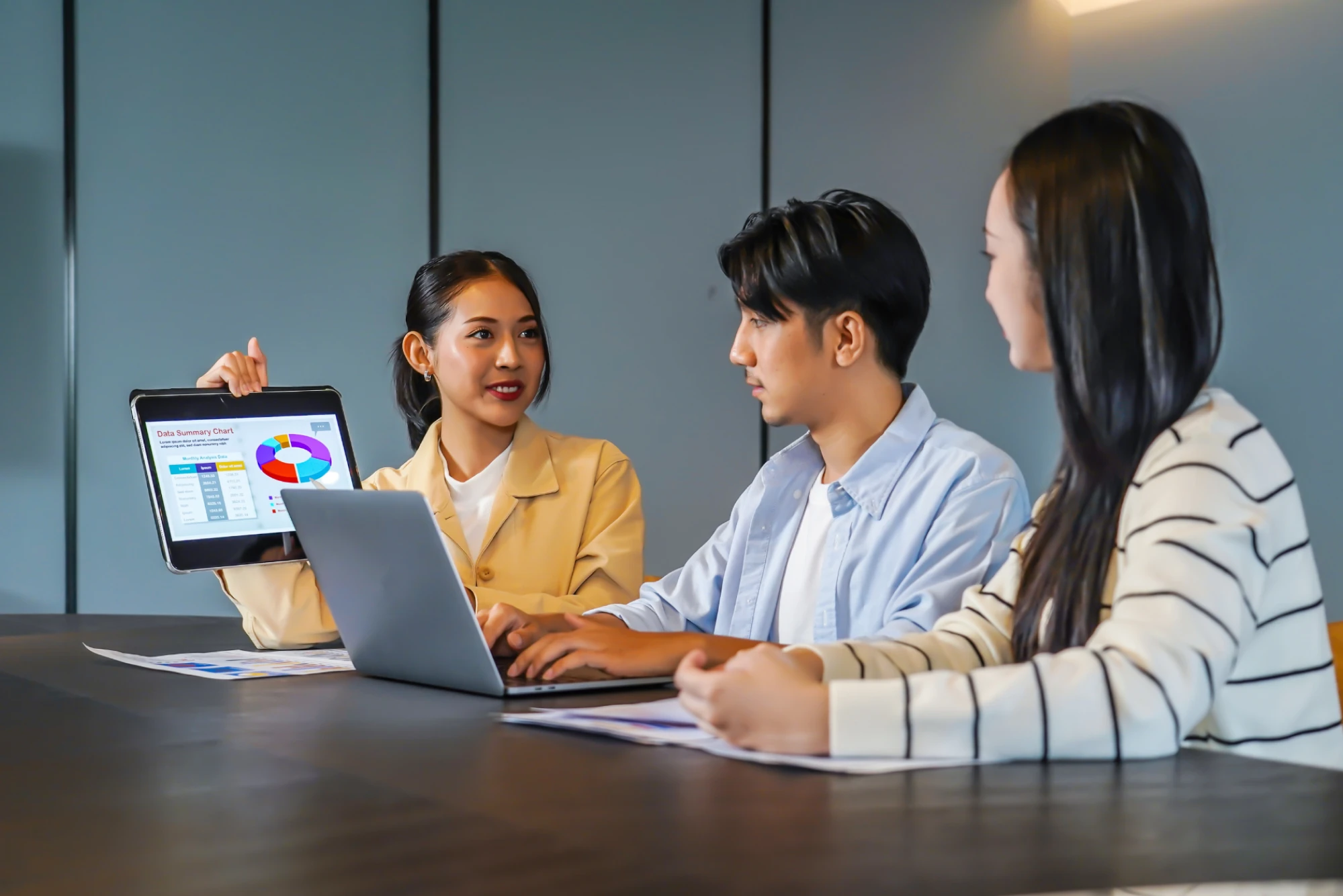 Three people are sitting at a conference table in a modern office, collaborating during a meeting