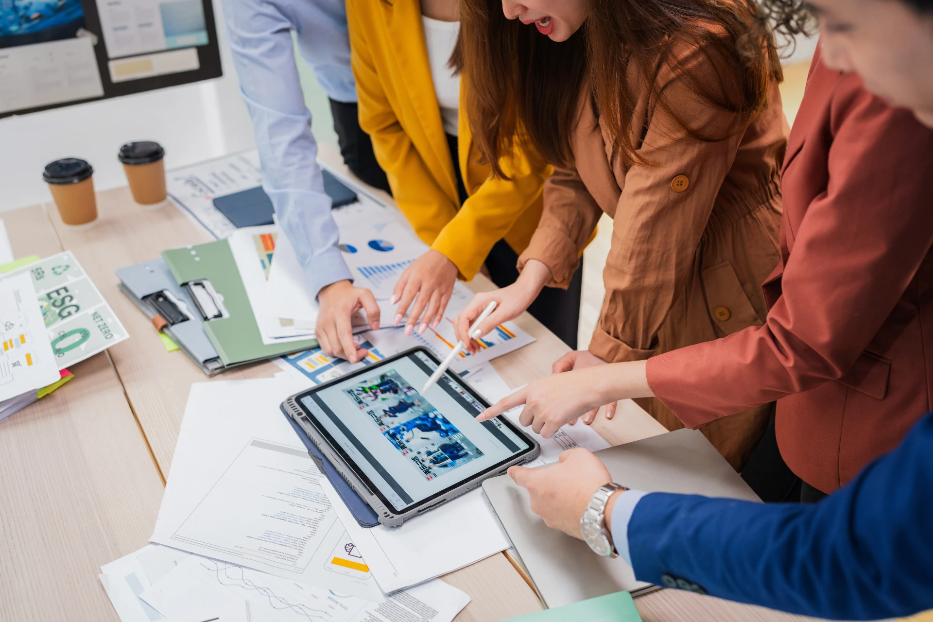 Team members collaborate around a table, reviewing charts and a tablet during a business meeting.