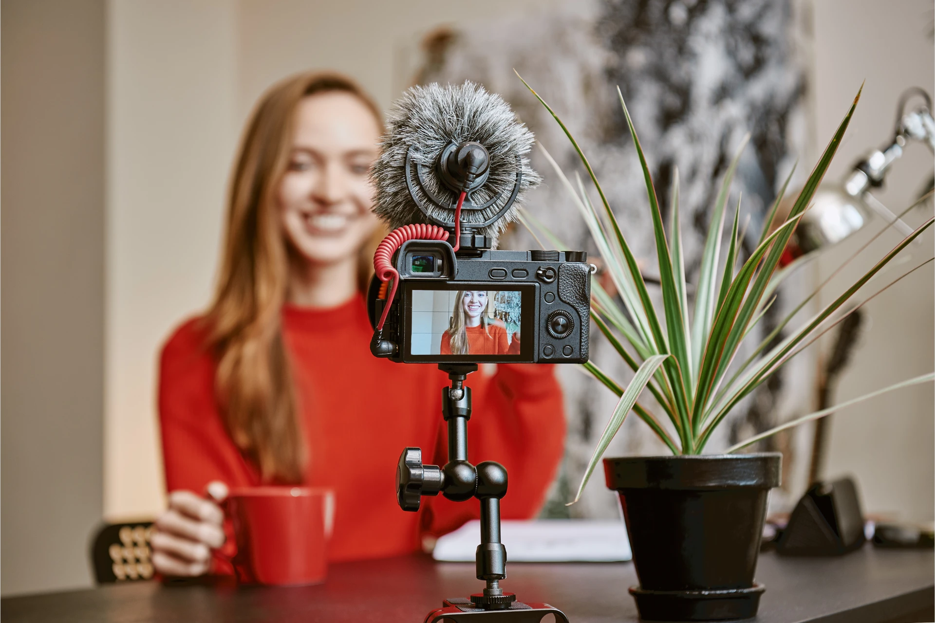 Cheerful female influencer making a new video for her vlog and drinking tea while sitting indoors.
