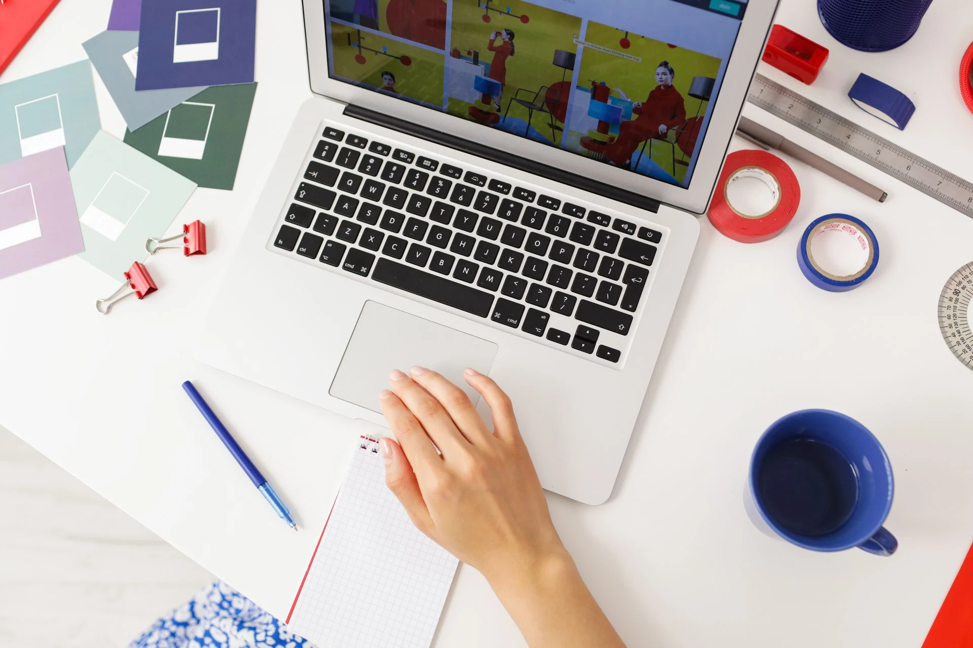 A creative workspace featuring a laptop, design tools, and a hand writing on a notepad