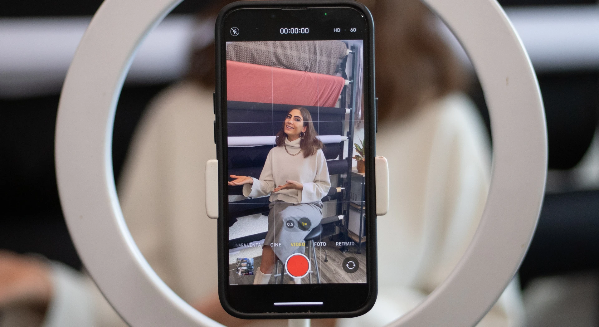 A woman recording short-form video content with a phone and ring light setup
