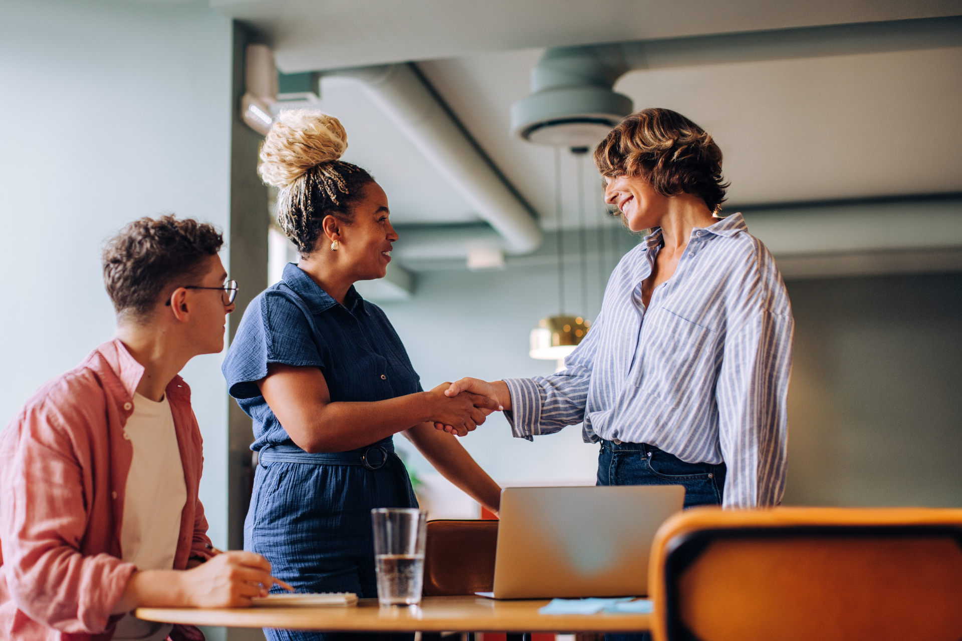 Three individuals interact in a professional setting, with one extending a handshake during their discussion